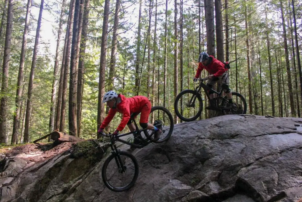 Green Course 2 Two adventure-seeking mountain bikers navigating the rugged trails of Squamish, honing their skills through exhilarating mountain bike lessons amid the stunning woodland scenery.